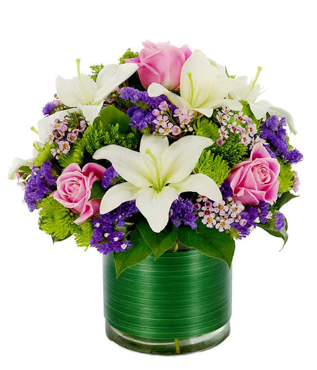 White asiatic lilies, purple statice and green poms in a circular glass vase