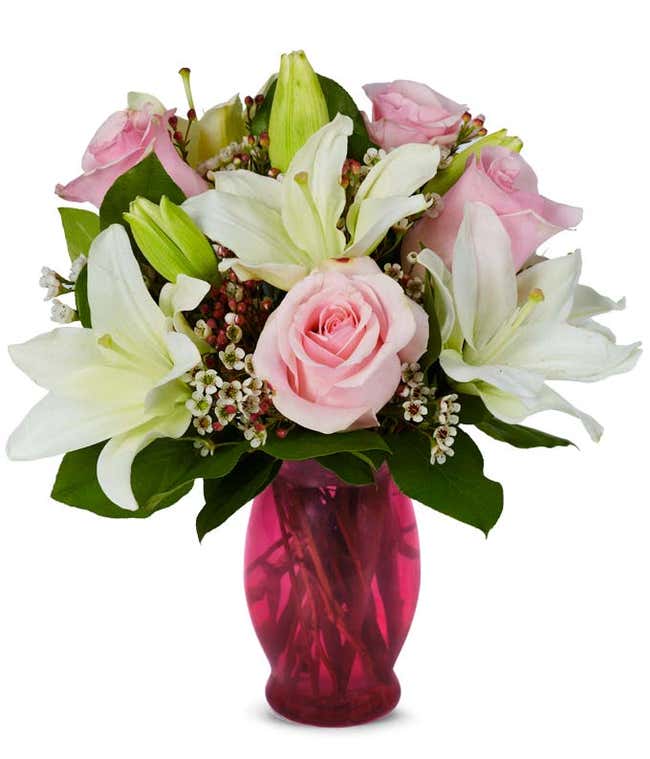 Light pink roses, white waxflowers and white lilies in a pink vase